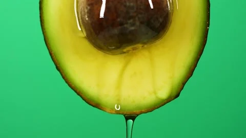 Slow motion close-up of fresh avocado fruit and oil flowing on green background Stock Footage 145471396