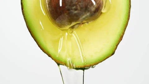 Slow motion close-up of fresh avocado fruit and oil flowing on white background Stock Footage 146879569
