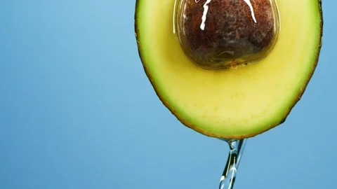 Slow motion close-up of fresh avocado fruit and oil flowing over blue background Stock Footage 147237953