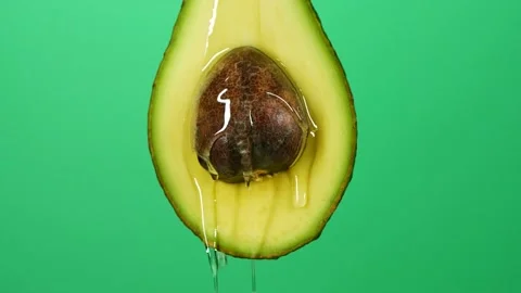Slow motion close-up of fresh avocado fruit and oil flowing on green background Stock Footage 148131085