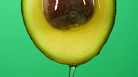 Slow motion close-up of fresh avocado fruit and oil flowing on green background Stock Footage 149090236