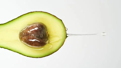 Slow motion close-up of fresh avocado fruit and oil flowing on white background Stock Footage 149550557