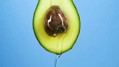 Slow motion close-up of fresh avocado fruit and oil flowing over blue background Stock Footage 150009797