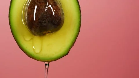 Slow motion close-up of fresh avocado fruit and oil flowing over pink background Stock Footage 150413278