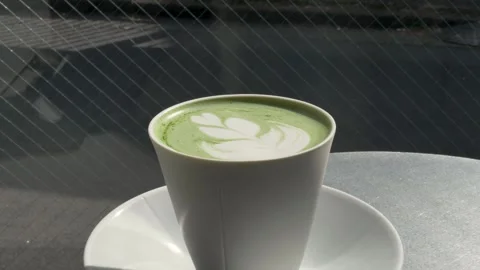 Slow motion close-up of a frothy green matcha hot drink with latte art in a cup Stock Footage 335923793