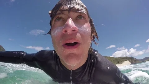 SLOW MOTION CLOSE UP: Happy young surfer doing duck dive Stock Footage 70496331