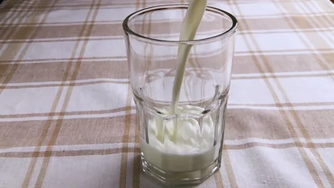 Slow motion close-up milk drink pouring into low glass standing on tablecloth. Stock Footage 130738678