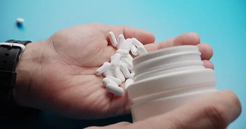 Slow motion close-up of pills poured into hand on blue background Stock Footage 307948903