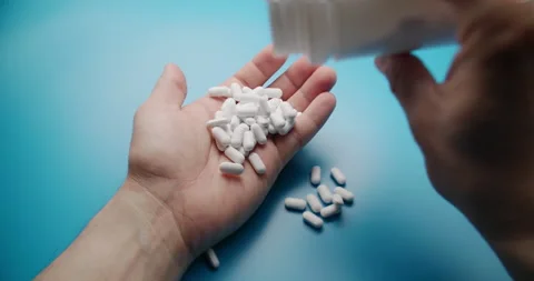 Slow motion close-up of pills poured into hand on blue background Stock Footage 307949161