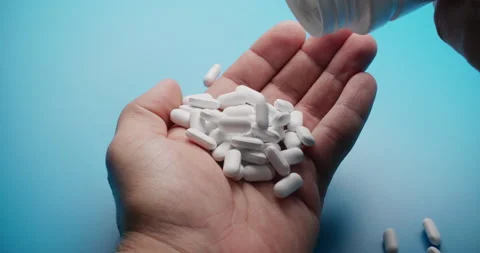 Slow motion close-up of pills poured into hand on blue background Stock Footage 307951425