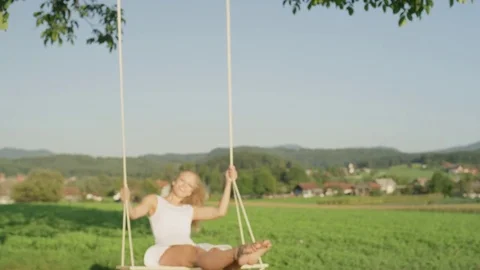 SLOW MOTION CLOSE UP PORTRAIT Smiling sunlit woman in white swinging under tree. Stock Footage 82624722