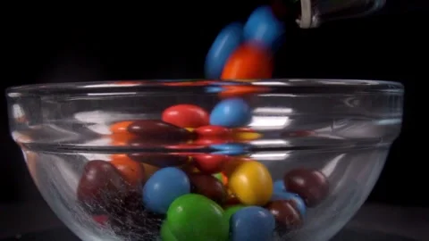 Slow motion close up of pouring peanut chocolate candies in clear glass bowl Stock Footage 279039526