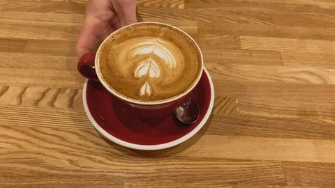 Slow motion. Close up. Red mug with a coffee on wood table. Coffee art latte cup Stock Footage 123553278