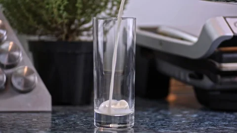 Slow motion close-up shot of milk cold beverage drink pouring into low glass in Stock Footage 104872761