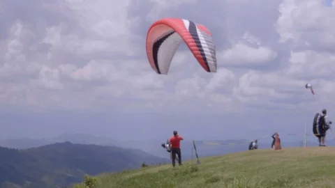 Slow motion close shot of para glider in group leaping off green hillside Stockbeeldmateriaal 102064715