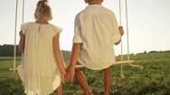 Slow Motion Close Up Shy Couple Of Young Kids Holding Hands On A Wooden Swing Stock Footage