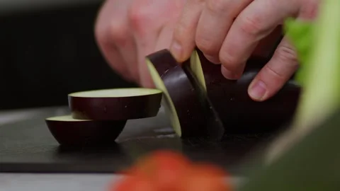 In a slow-motion close-up, the strong hands of a male chef cut an eggplant; the Stock Footage 273013131