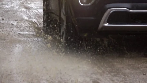 SLOW MOTION CLOSE UP: SUV car driving over deep rain puddle on dirt road