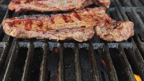 Slow Motion Close Up of Two Juicy Sirloin Steaks Sizzling on Black BBQ Grill Stock Footage 339217735