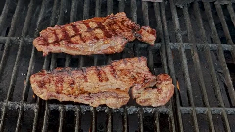 Slow Motion Close Up Two Juicy Sirloin Cuts Sizzling on Black BBQ Surface with Stock Footage 339217755