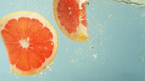 Slow motion close-up video of a piece of grapefruit falling into water. Video stock 263026430