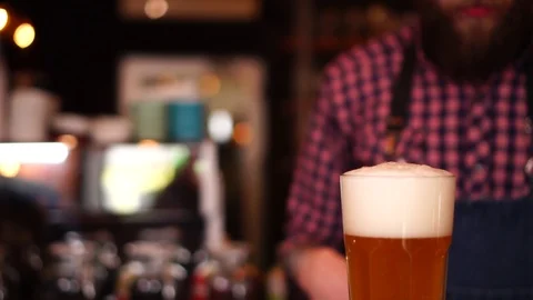 Slow motion close up view on foam lager beer pint glass and busy bartender on Stock Footage 103745046