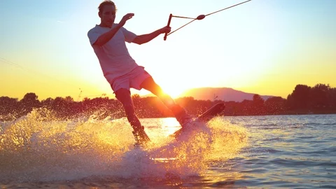 SLOW MOTION CLOSE UP: Young surfer wakeboarding and jumping 180 ollie at sunset Video stock 101000383