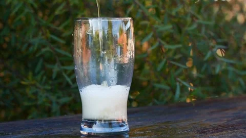Slow motion closeup pouring beer with foam and bubbles in glass on wooden table 스톡 동영상 261696283