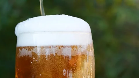Slow motion closeup pouring beer with foam and bubbles in glass on wooden table Stock Footage 261705155