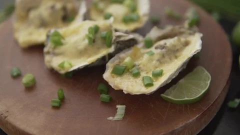 Slow motion closeup serving open oysters with cheese, green onion and lime in a 動画素材 91200864