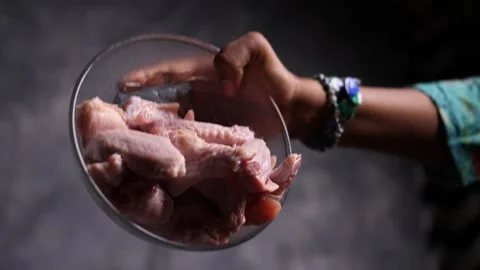 Slow motion closeup view of fresh chicken wings falling into a glass bowl Stock Footage 132976324