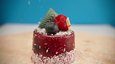 Slow motion coconut chips fall on the red dessert on the rotating table Stock Footage 148223411