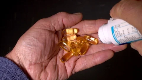 Slow motion: Cod liver oil capsules being tipped into palm of a man’s hand. Video stock 95774771