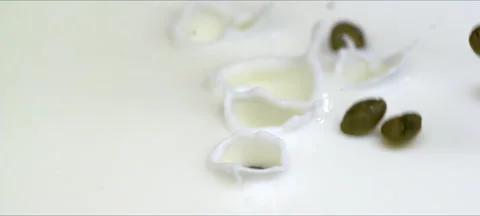 Slow-motion coffee beans falling into milk, creamy splash and swirl Stock Footage 323439881