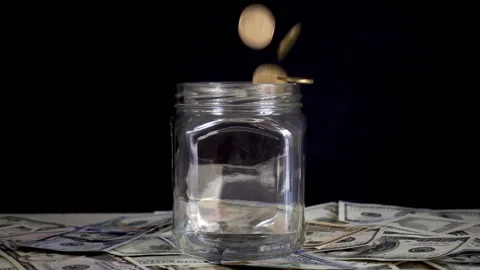 Slow motion, coins falls into an empty glass jar standing on dollar bills Stock Footage 93294457