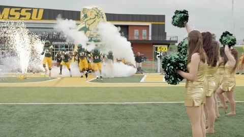 Slow-motion college football players break through paper pregame and run Stock Footage