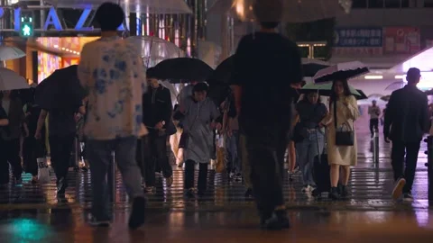 Slow motion of commuters walking with umbrellas across illuminated plaza Japan Stock Footage 331004508