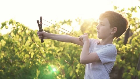 Slow motion a concentrated boy shooting wooden slingshot a pebble at a target Stock Footage 91750367