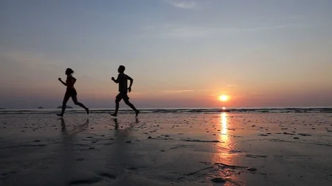 Slow motion of couple joogging on beach, runners silhouettes Stock Footage 98092861