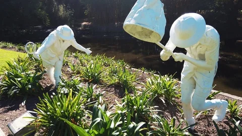 Slow motion crane up reveal of two white statues by pond Video stock 108968758