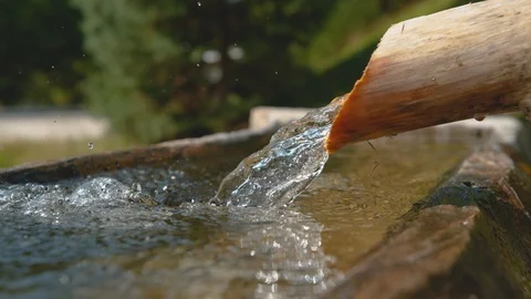 SLOW MOTION: Crystal clear stream water flows through the wooden pipe into basin Stock Footage 99012078