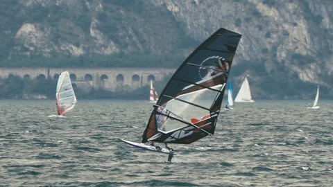 Slow motion CU windfoil windsurfer on Lake Garda with mountains in background Stock Footage 117833199