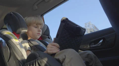 Slow motion. Cute 5 years old boy plays tablet during a trip in a car. Stock Footage 280543946