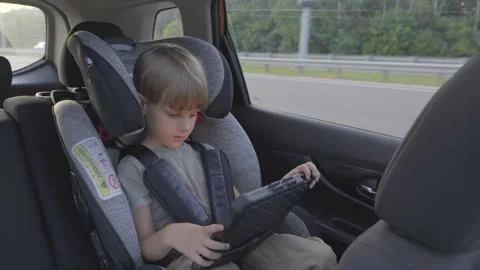 Slow motion. Cute 5 years old boy plays tablet during a trip in a car. Stock Footage 280544132