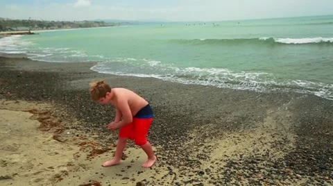 Slow motion of cute kid picking up sand at the beach by ocean Stock Footage 63750009