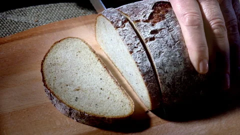Slow motion. Cutting dark bread into slices with a bread knife on a wooden board Stock Footage 295368945