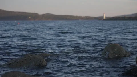 Slow Motion Deep Blue Waves and Distant Blurred White Lighthouse at Sunset in Stock Footage 344138951