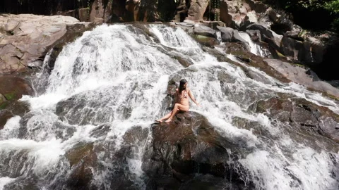 Slow motion drone footage pulling away from an Asian women siting in a waterfall Stock Footage 144357253
