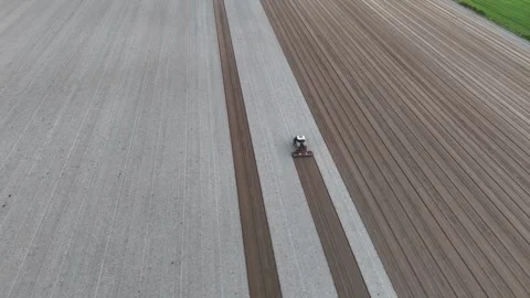 Slow-motion drone orbit over tractor leveling striped fields at Maginot Stock Footage 308443389