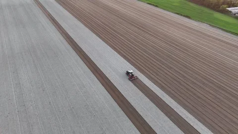 Slow-motion drone orbit of tractor drawing precise brown seed rows across pale Stock Footage 310180249